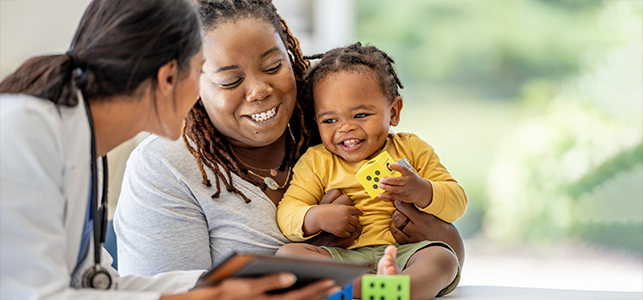 Pediatrician holding a tablet and smiling at mom and baby