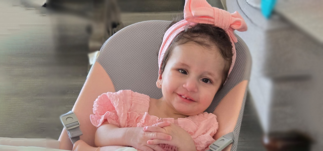 CHoR patient Alana smiling in her highchair with a pink bow in her hair
