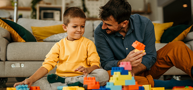 Young boy and his father play with blocks on the living room floor