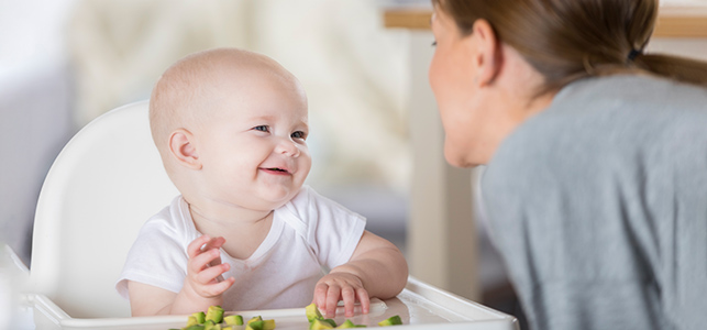 Baby smiling at mom with avocado on highchair try