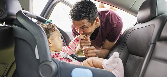 Father kissing his baby's hand as he puts her in car seat