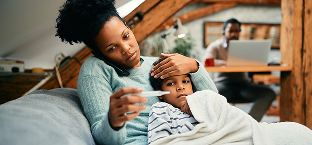 Mother checking son's temperature while snuggling on sofa
