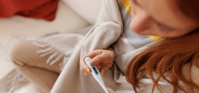 Teen girl wrapped in a blanket looks at thermometer