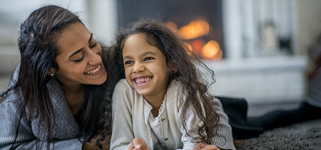 Mom and daughter snuggle and laugh near gas fireplace