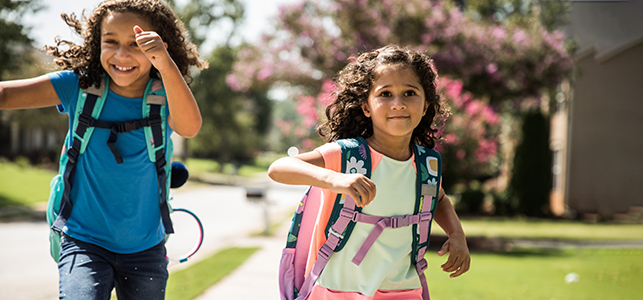 Two sisters wearing backpacks running home from school