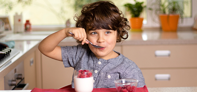 Child smiling at table with yogurt and raspberries