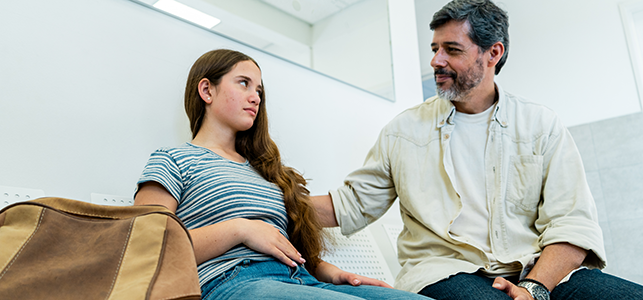 Dad comforting teen daughter while she holds her stomach