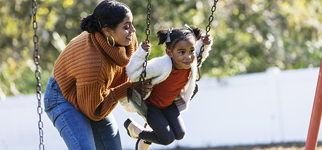 Mom pushing her young daughter on a swing