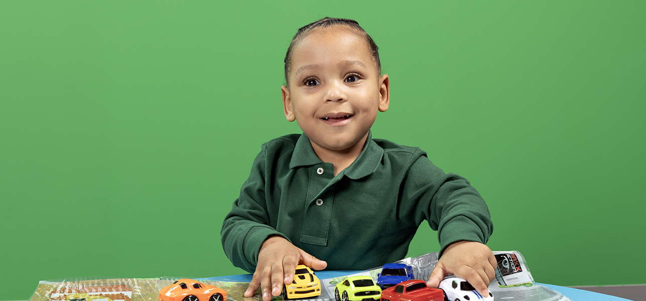 CHoR calendar kid Lennox playing with cars in front of green wall