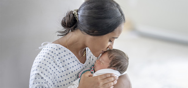 Mother in hospital gown kissing newborn baby