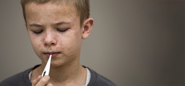 Boy with measles on his face taking temperature