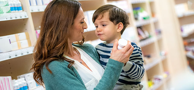 Mom looks at a medicine bottle while holding her son at the pharmacy