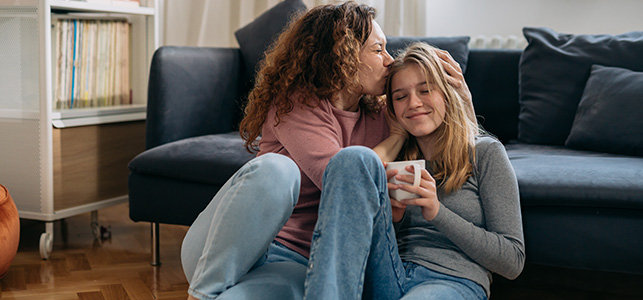Mom kissing head of teen daughter on living room floor