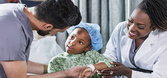 Male nurse talking to a pediatric patient in hospital gown and cap