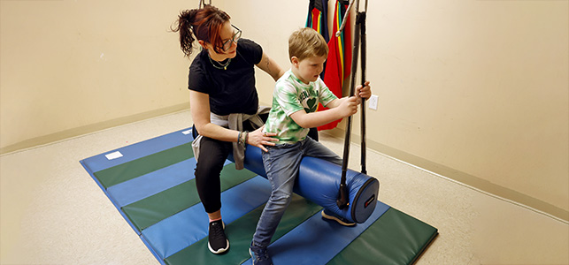 A boy and his CHoR therapist on a blue bolster swing
