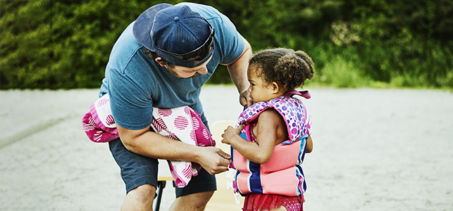 Dad putting a life jacket on his young daughter at the beach
