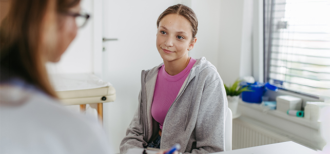 Adolescent girl in pink shirt talking to her doctor