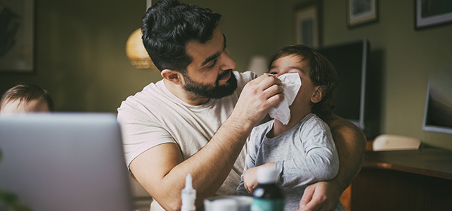 Dad helping small child blow nose at home