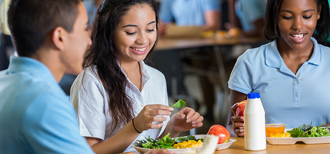 Three adolescent students eat salad in the school cafeteria