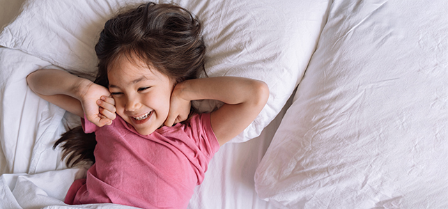 Girl wearing pink shirt smiling as she wakes up in bed