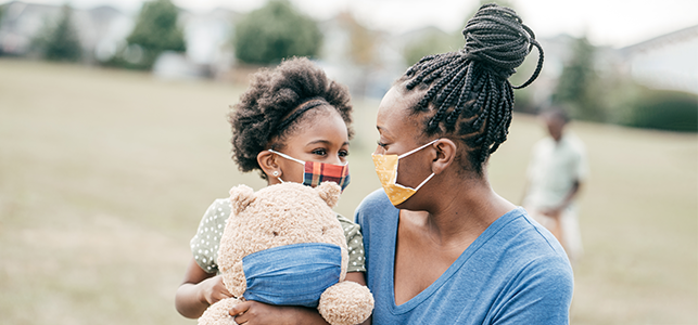 Mother, daughter and teddy bear outside wearing masks