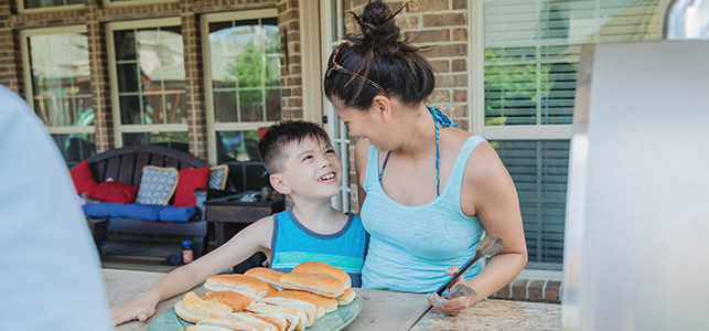 Boy and his mom smiling with plate of hot dogs at summer cookout