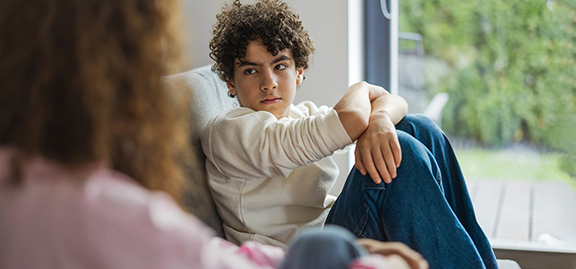 Anxious teen boy with curly hair talking to his mom on the sofa