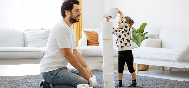 Toddler and her dad stacking rolls of toilet paper in the living room
