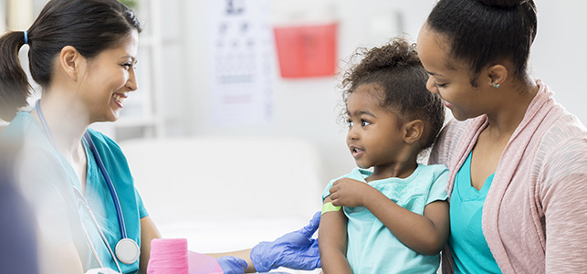 Young girl sitting on mother's lap receiving a bandaid after vaccination