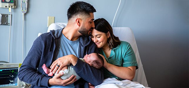 Parents snuggling with their newborn baby on a hospital bed