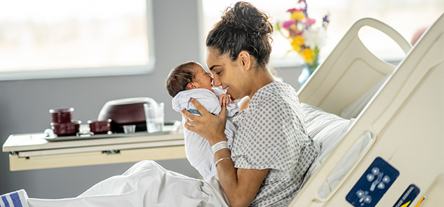 Mother smiling and holding newborn baby face-to-face in hospital bed
