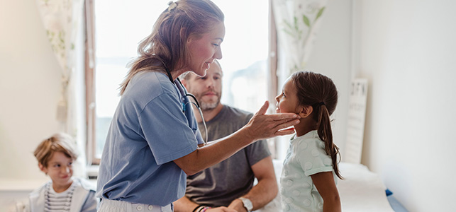 Pediatric nurse examines girl's neck while dad looks on