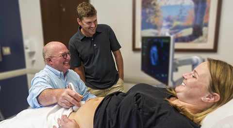 Dr. Lucidi providing ultrasound for pregnant woman while sitting next to smiling dad