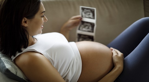 Pregnant woman holding belly and smiling while holding ultrasound photos